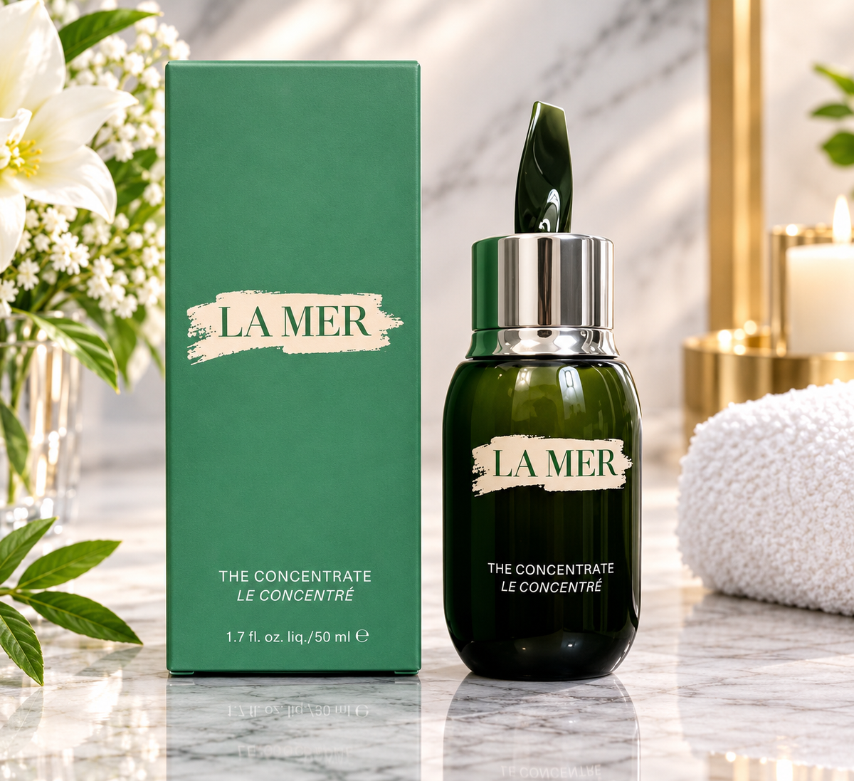 La Mer The Concentrate Le Concentré bottle in dark green glass with a silver cap next to its green box, displayed on a marble surface with white flowers and a towel in the background.
