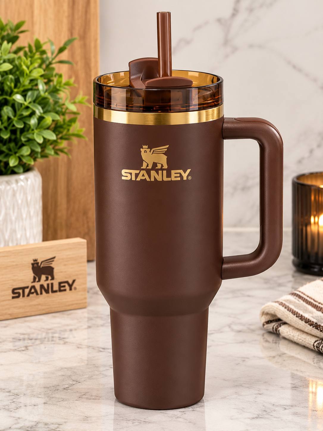 Stanley brown insulated travel mug with a handle, lid, and straw, shown on a marble countertop with branded blocks and home decor in the background.