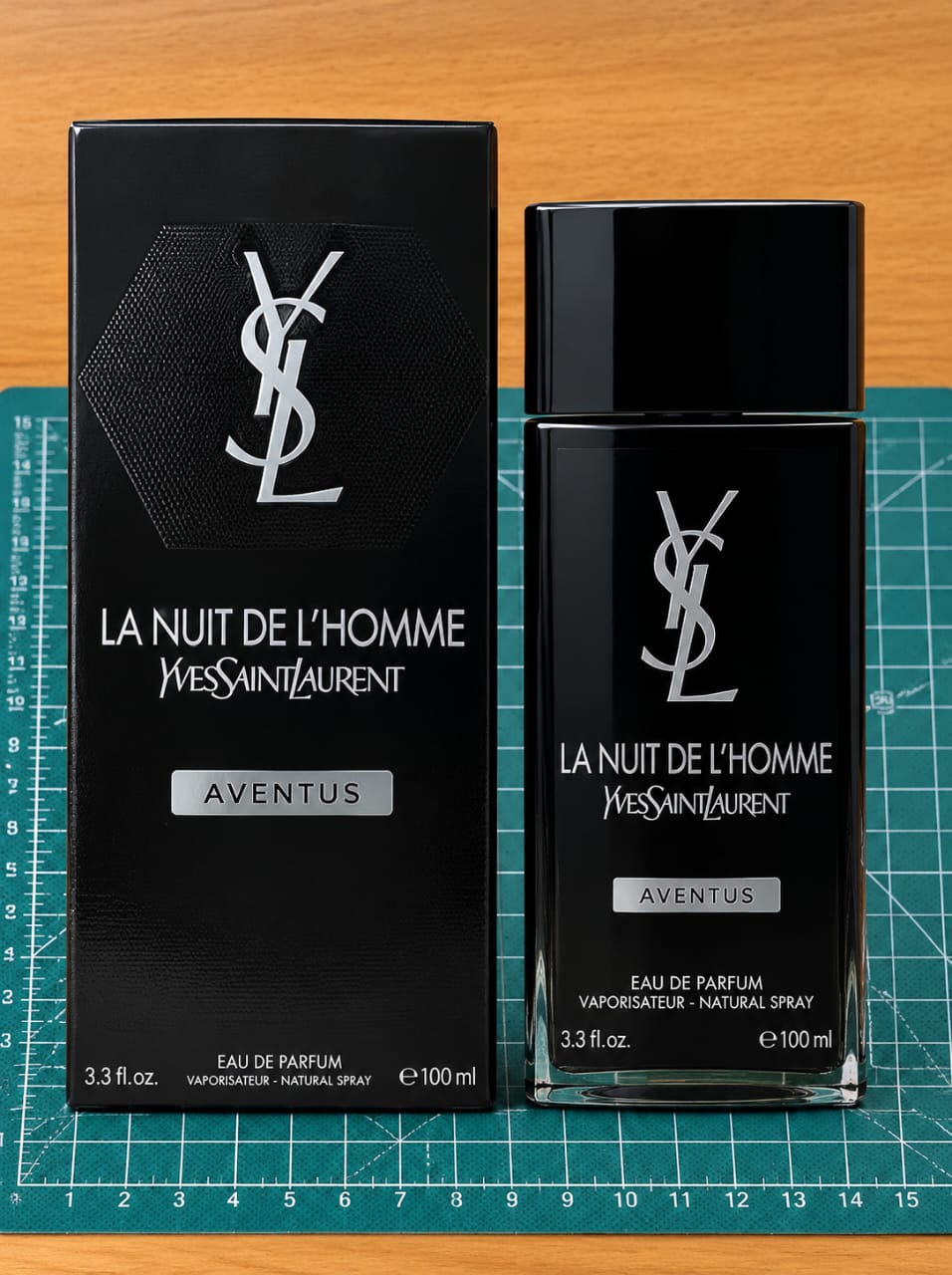 Yves Saint Laurent La Nuit de L'Homme Aventus Eau de Parfum 100ml bottle and its black packaging box, displayed on a green cutting mat over a wooden surface.